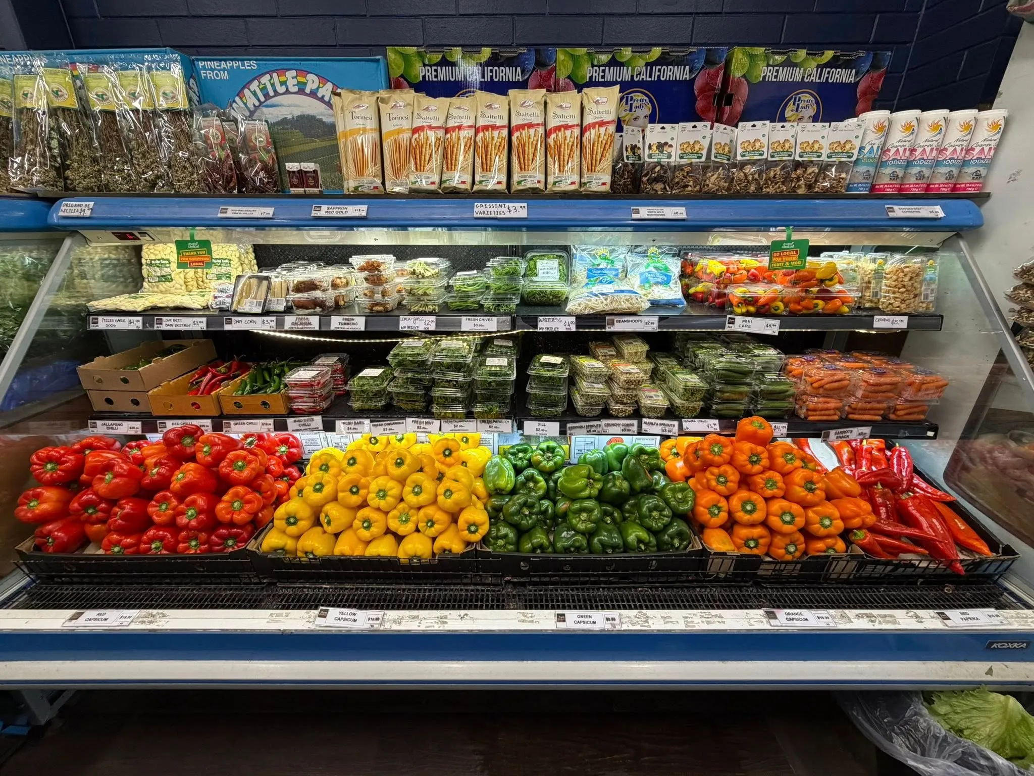 Refrigerated case with colourful bell peppers, herbs and prepared items