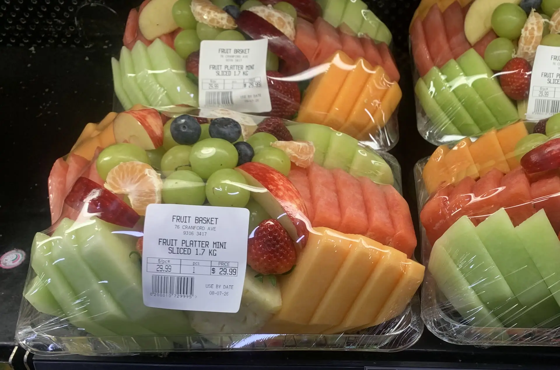 Sliced fruit platter trays with strawberries, melon, grapes and blueberries in the cold case