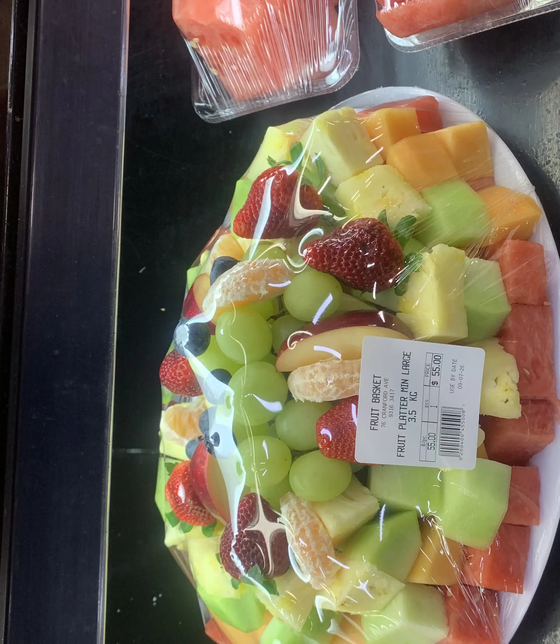 A wrapped sliced fruit platter on a plate, ready to travel